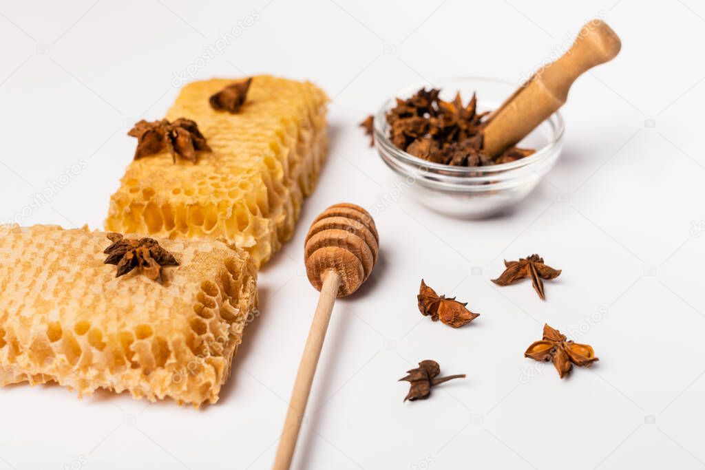 honey dipper, bowl with wooden scoop and anise seeds near honeycomb on white