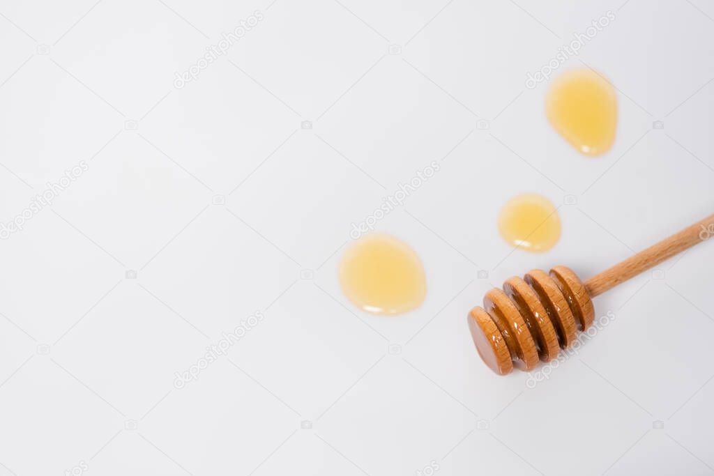 top view of wooden dipper near honey drops on white background with copy space