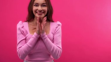 Şaşırmış ve heyecanlı bir kadın pembe üzerinde el çırpıyor.