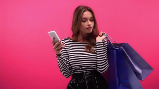 Attente Vrouw Met Boodschappentassen Met Behulp Van Smartphone Geïsoleerd Roze — Stockvideo