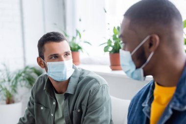 multiethnic men in medical masks talking in hospital, vaccination concept clipart