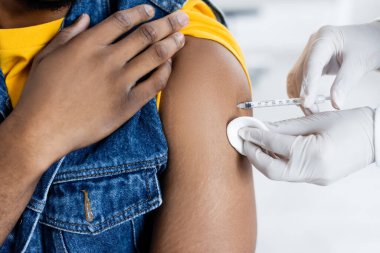 Lateks eldivenli doktor, Afrikalı Amerikalı bir adamı klinikte aşılıyor.