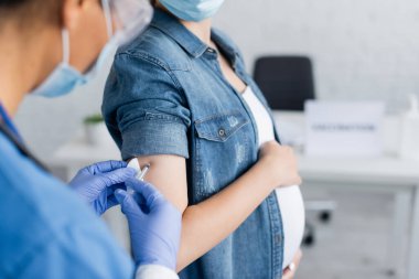 Klinikte hamile kadını aşılayan bulanık hemşire görüntüsü.
