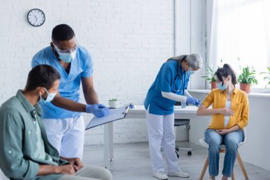 Tıp maskeli ve üniformalı çok ırklı doktorlar aşı merkezinde hastalarla birlikte çalışıyorlar.