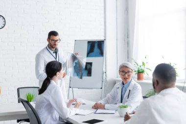 Konsey sırasında çok ırklı meslektaşlarına ciğerlerinin röntgenini gösteren genç bir doktor.