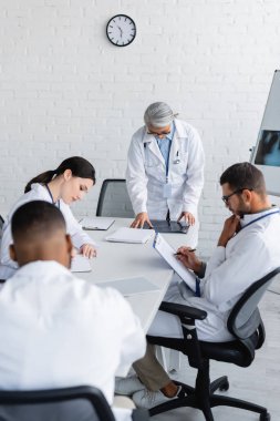 Konsey sırasında çok ırklı meslektaşlarının yazdığı röntgenlere bakan orta yaşlı Asyalı doktor