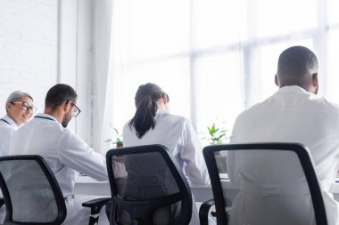 Gözlüklü, gülümseyen Asyalı doktorun yakınındaki çok ırklı doktorların arka planı  