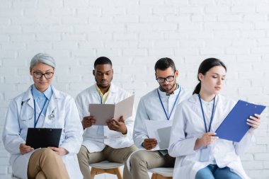 Beyaz önlüklü çok ırklı doktorlar konferans sırasında belgelere bakıyorlar.
