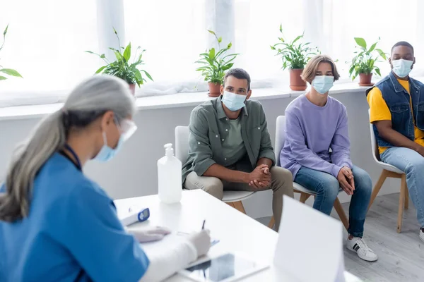 Suddig Sjuksköterska Skriver Nära Multietniska Personer Medicinska Masker Väntar Vaccinationscenter — Stockfoto