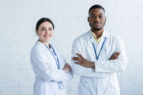 Positive Multiethnische Ärzte Weißen Kitteln Stehen Mit Verschränkten Armen Und — Stockfoto