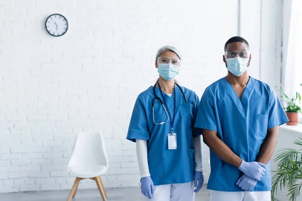 Multikulturní Lékaři Uniformách Lékařských Maskách Při Pohledu Kamery Vakcinačním Centru — Stock fotografie