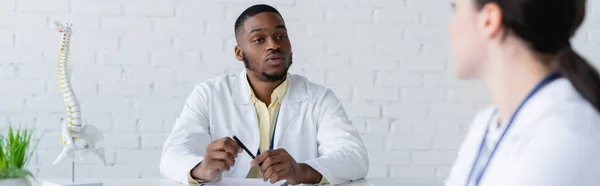 Médico Afroamericano Sosteniendo Pluma Mientras Habla Con Colega Borroso Pancarta — Foto de Stock