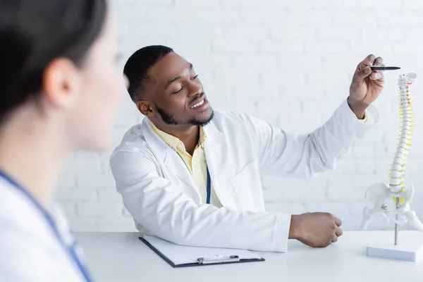 Sorridente Africano Americano Médico Apontando Com Caneta Modelo Coluna Vertebral — Fotografia de Stock