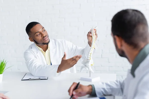 African American Physician Pointing Spine Model Blurred Colleague — Stock Photo, Image