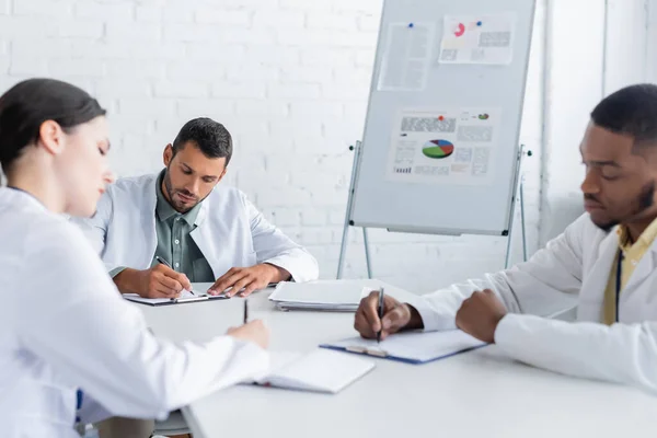 Médicos Multiculturais Escrevendo Sala Conferências Perto Flip Chart Com Infográficos — Fotografia de Stock