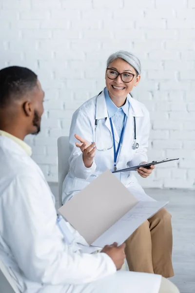 Feliz Asiático Médico Apuntando Con Mano Mientras Habla Borrosa Africano — Foto de Stock