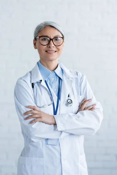Dojrzały Azjatycki Lekarz Białym Płaszczu Okularach Stojących Skrzyżowanymi Ramionami Uśmiechających — Zdjęcie stockowe