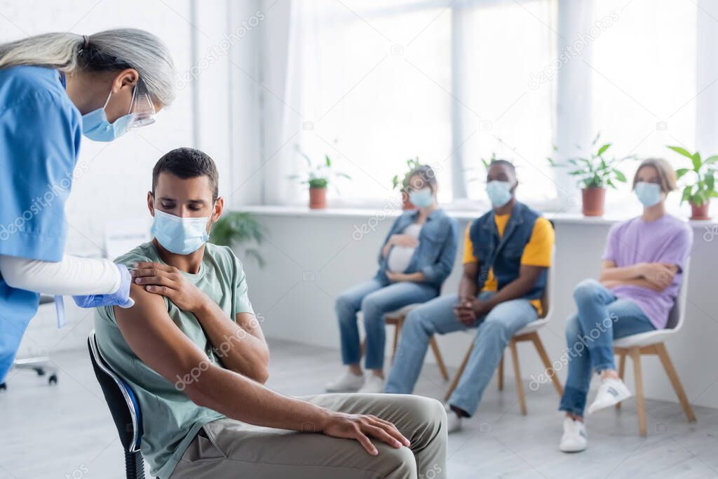 middle aged asian nurse giving vaccine injection to young man and patients in medical masks