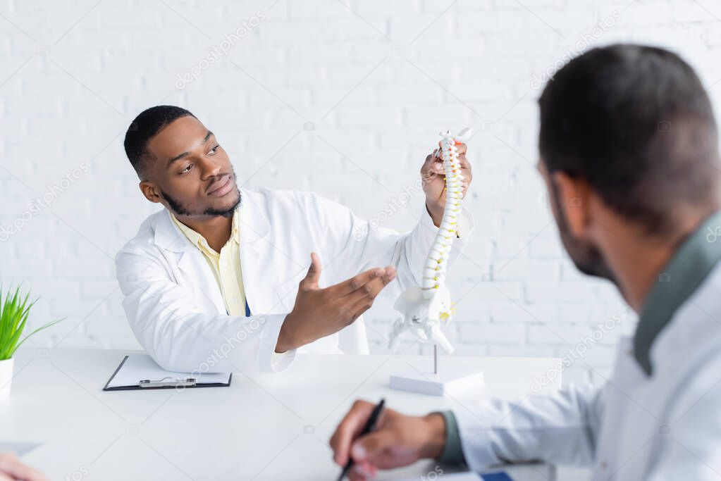 african american physician pointing at spine model near blurred colleague