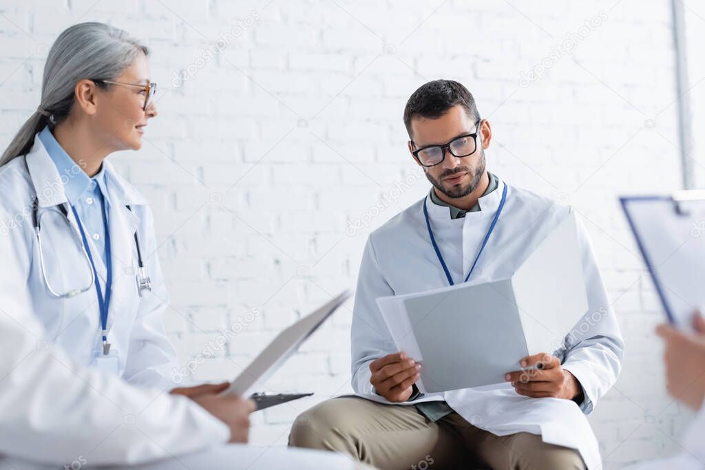 middle aged asian doctor talking to young colleague looking at documents during council