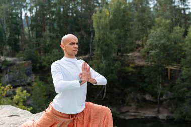 Beyaz kazak giyen Budist ormanda dua eden ellerle yoga yapıyor.