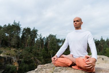 Kapüşonlu Budist dışarıda meditasyon yaparken başka tarafa bakıyor.