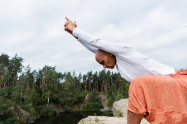 Beyaz tişörtlü Budist yoga pozunda meditasyon yapıyor açık havada elleri havada.