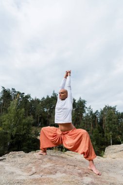 Harem pantolonu ve sweatshirt giymiş Budist, tanrıça pozunda ellerini kaldırarak meditasyon yapıyor.