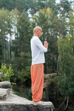 Tişörtlü ve harem pantolonlu Budist 'in açık havada dua eden elleriyle meditasyon yapmasını uzun süre izlemek.