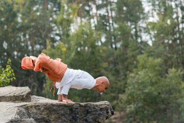 Harem pantolonlu Budistin kaldırılmış nilüferde meditasyon yaparken kayalık kayalıklarda duruşu.