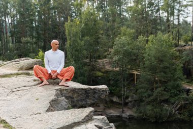 Çıplak ayaklı Budist Orman Gölü 'nün üzerindeki kayalık kayalıklarda otururken meditasyon yapıyor.