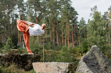 Yarım ayda yoga yapan çıplak ayaklı Budist ormanda kayalıklarda poz veriyor.
