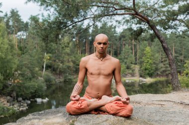 Dövmeli, üstsüz Budist Lotus pozunda meditasyon yapıyor açık havada gözleri kapalı.