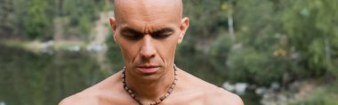 Boncuklu üstsüz Budist açık havada meditasyon yapıyor, afiş yapıyor.