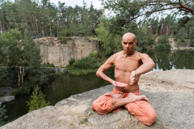 Üstsüz Budist hareketleriyle yoga yaparken suyun üzerindeki kayalık kayalıklarda poz veriyor.