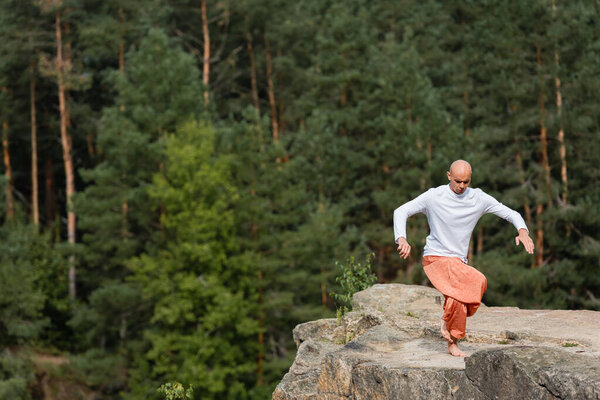 barefoot buddhist meditating in yoga pose on rocky cliff in forest