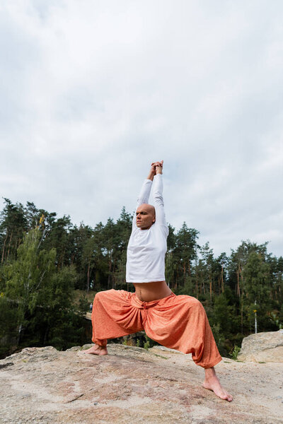 buddhist in harem pants and sweatshirt meditating with raised hands in goddess pose