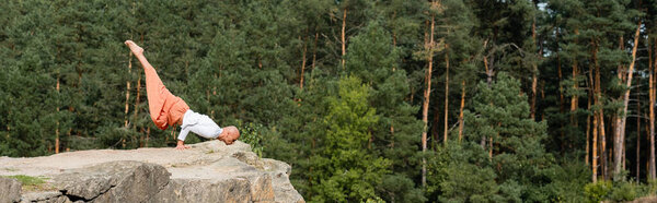 side view of buddhist in arm balancing pose on rock in forest, banner