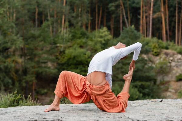 barefoot buddhist practicing crocked monkey pose in forest