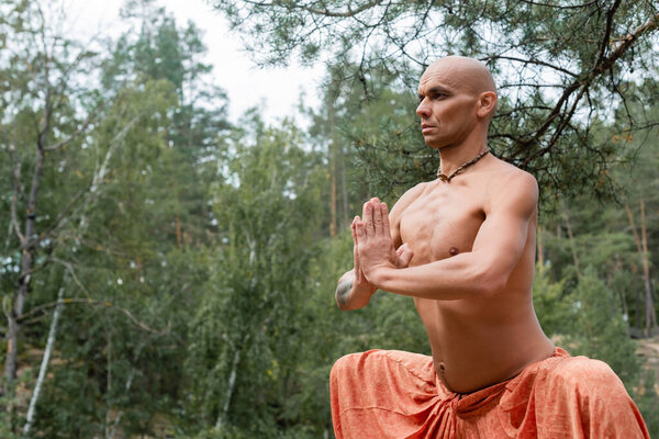 shirtless buddhist meditating in yoga pose with praying hands outdoors