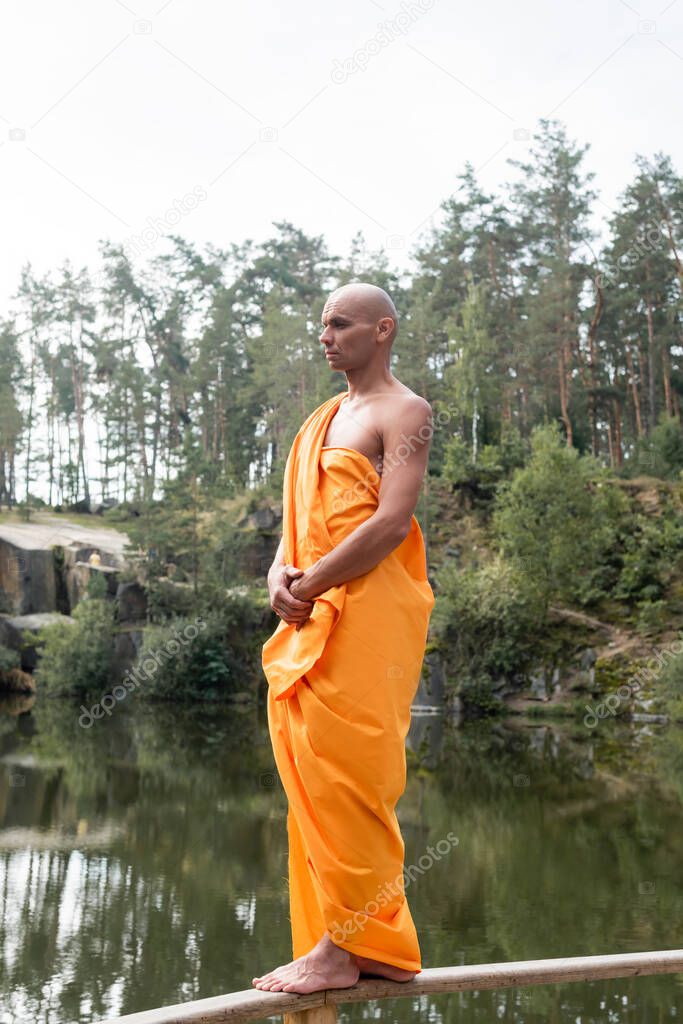 full length view of barefoot buddhist meditating while standing on wooden fence