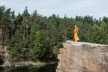 Turuncu cüppeli Budist 'in nehir üzerindeki kayalık kayalıklarda meditasyon yapmasını uzun süre izleyebilirsiniz.