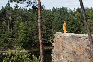 Turuncu kasaya giymiş Budist keşiş ormandaki yüksek kayalıklarda dua ediyor.