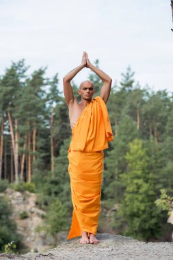 Turuncu kasaya giymiş, ormanda dua eden ellerle meditasyon yapan Budist 'i uzun süre görmek.