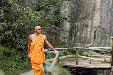 Geleneksel Budist cüppeli bir adam ormandaki ahşap çitlerin yanında yürüyor.