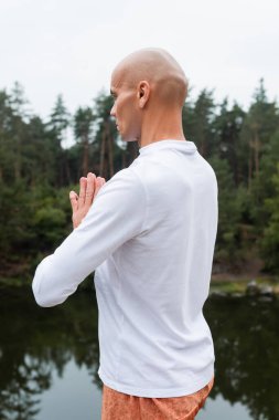 buddhist in white sweatshirt praying and meditating outdoors clipart