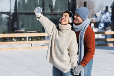 happy couple sticking out tongues while taking selfie on ice rink  clipart