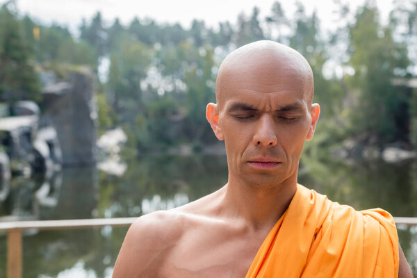 Буддийский монах молится с закрытыми глазами на открытом воздухе