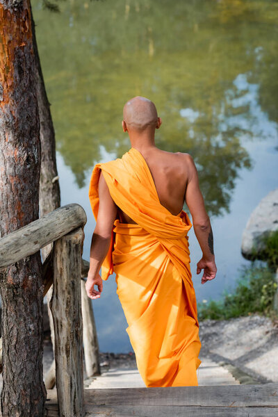 задний вид буддийского монаха, идущего по лестнице в лесу возле озера