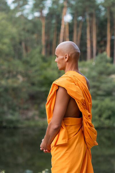 man in traditional buddhist robe meditating in forest